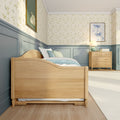 Cozy kids bedroom with light wood bed, pale blue wainscoting, floral wallpaper, wooden dresser and bedside lamp in soft pastel decor