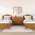 Kids' bedroom with matching wooden twin beds, pink bedding and pillows, plush teddy bears, floral wallpaper, framed pink poodle artwork and bedside lamp on a wooden nightstand