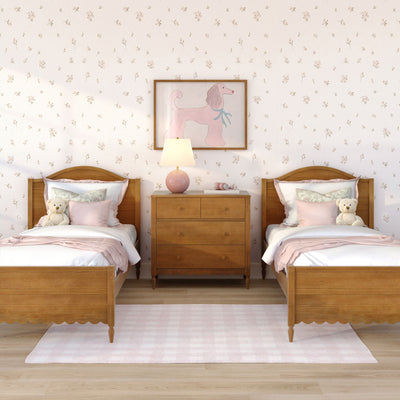 Kids' bedroom with matching wooden twin beds, pink bedding and pillows, plush teddy bears, floral wallpaper, framed pink poodle artwork and bedside lamp on a wooden nightstand