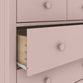 Soft pink wooden dresser drawer close-up with round knob, visible dovetail joinery and metal drawer slide