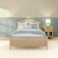 Cozy farmhouse bedroom with light wood bed, pastel blue bedding, delicate floral wallpaper, blue-gray wainscoting and bedside lamp