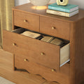 Solid wood mid-century dresser with open drawer revealing folded blankets, brass knobs, lamp and stacked books on top — bedroom storage and decor