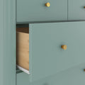 Close-up of a modern teal dresser with gold knobs and an open wooden drawer revealing metal drawer slides, contemporary bedroom furniture