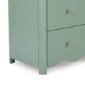 Close-up of mint green wooden dresser corner with brass knob and scalloped base, modern nightstand