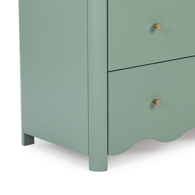Close-up of mint green wooden dresser corner with brass knob and scalloped base, modern nightstand