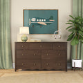 Dark wood dresser with brass knobs beneath framed teal airplane wall art, ceramic table lamp, headphones on a gold stand, potted fiddle‑leaf fig and green curtains