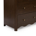 Dark walnut dresser close-up with brass knobs, visible wood grain and scalloped base on a bedroom chest of drawers