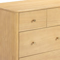 Close-up of light natural wood dresser with smooth rounded top edge and brass cone drawer knobs, modern minimalist chest of drawers