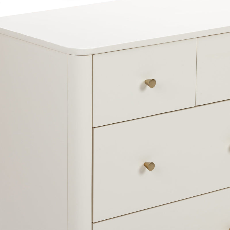 Close-up of a white modern dresser corner with rounded top edge and brass knob, minimalist bedroom nightstand drawers in matte cream finish