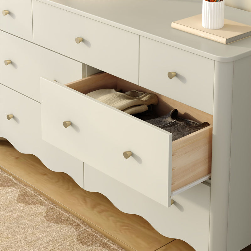 White wooden dresser with open drawer showing folded sweaters, brass knobs and light wood interior — bedroom storage furniture