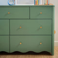 Green painted dresser with gold knobs on hardwood floor, topped with a blue alarm clock and colorful wooden abacus — mid-century modern kids' bedroom storage piece