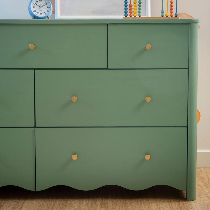 Green painted dresser with gold knobs on hardwood floor, topped with a blue alarm clock and colorful wooden abacus — mid-century modern kids' bedroom storage piece