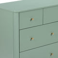 Close-up of matte sage green painted wooden dresser with brass cone drawer knobs, modern bedroom storage chest
