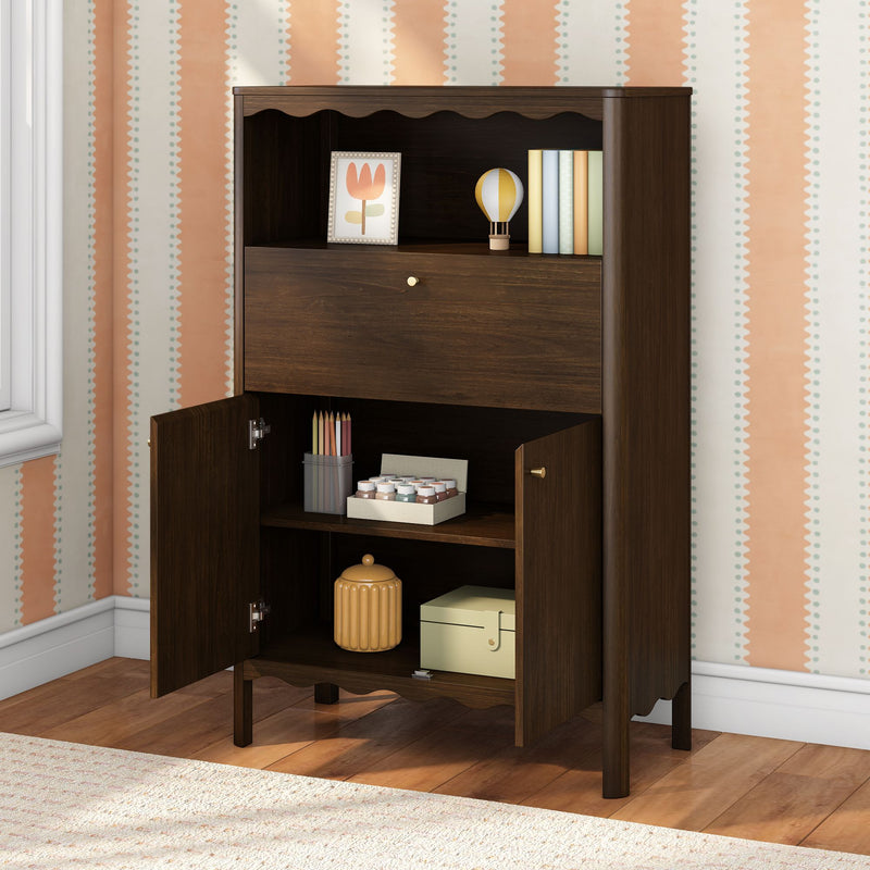 Dark walnut storage cabinet in nursery with open shelves showing framed tulip print, pastel books, wooden hot air balloon toy, colored pencils and craft paint jars against peach striped wallpaper.