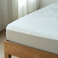 Close-up of white textured mattress with quilted cover on wooden bed frame in bright minimalist bedroom