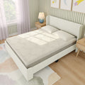 Upholstered platform bed with textured cream mattress and two pillows in a light green striped bedroom with wooden nightstands, blue lamp, pastel watercolor rug and sunlight from window