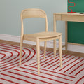 Light wooden chair beside matching desk in minimalist Scandinavian home office with red spiral lamp and red-striped rug