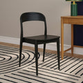 Modern black wooden dining chair next to a light oak side table with a green lamp on a black-and-white striped rug in a minimalist interior.