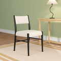 Minimalist modern dining chair with cream upholstery and black frame beside a natural wood side table and curved black table lamp against a sage green wall, hardwood floor and striped neutral rug