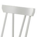 Close-up of white painted spindle-back wooden dining chair showing curved top rail and vertical spindles, modern farmhouse style