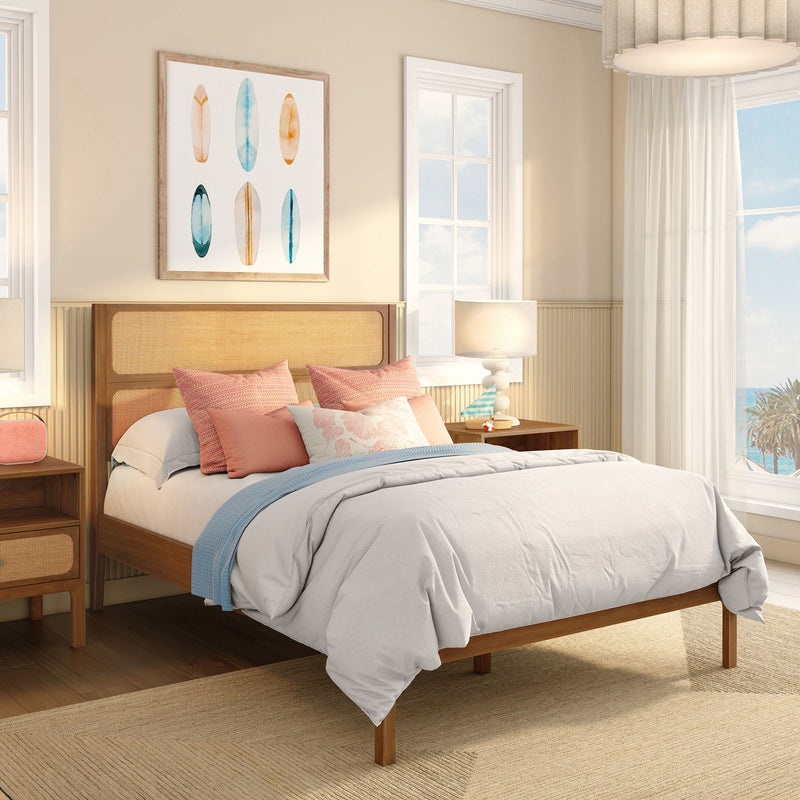 Coastal bedroom with rattan headboard, pastel coral and blue pillows, white bedding, surfboard wall art and ocean-view window