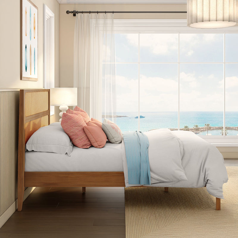 Coastal bedroom with ocean view, wooden bed frame, pastel throw pillows, sheer curtains and beach-facing window letting in natural light