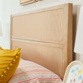 Close-up of natural wood rattan cane headboard with woven cane panel, yellow pom-pom pillow and striped bedding — boho bedroom decor