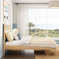 Coastal ocean-view bedroom with light wood bed, yellow-striped bedding, sheer curtains, palm tree view and coastal wall art
