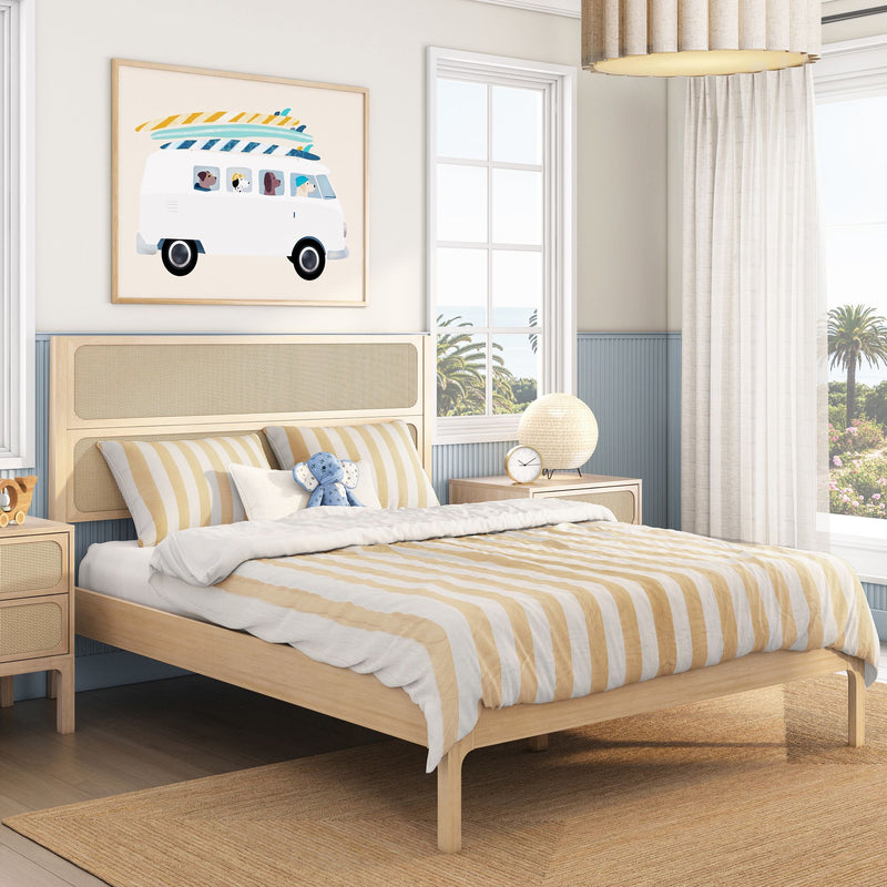 Coastal kids bedroom with light wood platform bed and rattan headboard, yellow-striped bedding, surf-van wall art, bedside lamp and palm-tree window view