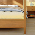 Close-up of wooden bed frame in modern bedroom, cozy neutral bedding with textured throw, bedside nightstand with glass lamp and stacked books