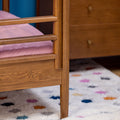 Close-up of mid-century modern wooden bed frame slats and leg with pink mattress and colorful polka-dot rug underneath