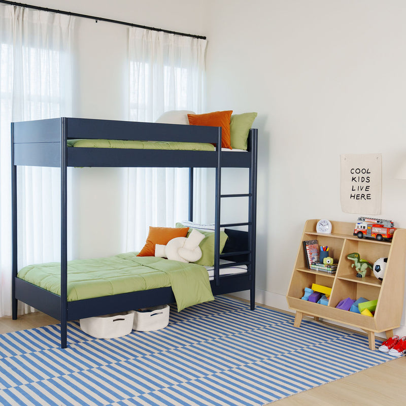 Modern navy metal bunk bed with green bedding and orange pillows in a bright kids' bedroom featuring a toy shelf, soccer ball and blue striped rug under sheer white curtains