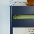 Close-up of a navy blue wooden bunk bed top bunk with green bedding, striped pillow and teddy bear in a modern kids' bedroom décor
