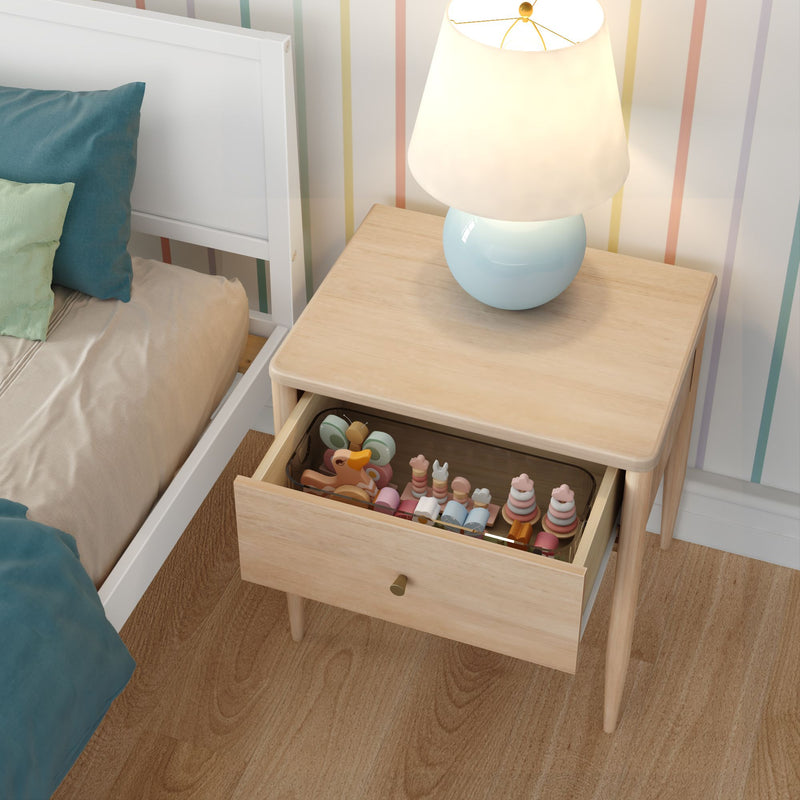 Modern light wood nightstand with round blue lamp and open drawer filled with wooden toys beside child's bed in pastel-striped nursery.