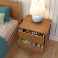 Wooden bedside nightstand with blue ceramic table lamp and two open drawers filled with colorful children's books and toys next to a wooden bed in a striped kids' bedroom