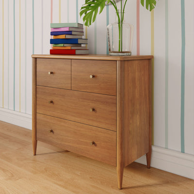 Mid-century modern wooden dresser on hardwood floor with stacked colorful books and clear glass vase holding monstera leaves against pastel striped wallpaper
