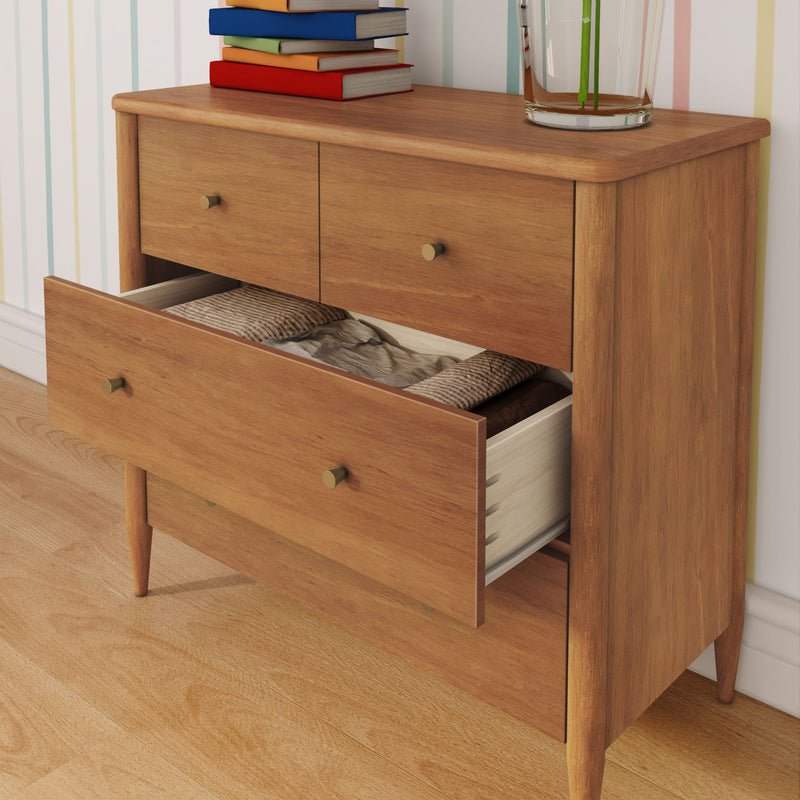 Mid-century modern wooden dresser with open drawer revealing folded linens, brass knobs, stacked books and glass vase against striped wallpaper on hardwood floor
