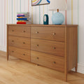Mid-century modern six-drawer oak bedroom dresser on hardwood floor against pastel striped wallpaper, styled with a blue table lamp, small clock and stack of colorful books for bedroom storage and decor