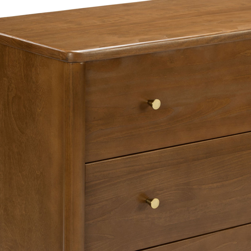 Close-up of a mid-century modern honey-brown wooden dresser with smooth wood grain, round brass knobs and stacked drawers for bedroom storage