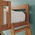 Close-up of solid wood bunk bed ladder and guardrail with white bedding against a teal bedroom wall, oak finish