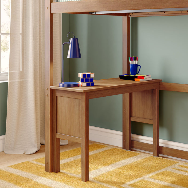 Wooden loft-bed study desk with blue desk lamp, Rubik's Cube, mug of colored pens and stacked books against a sage green wall and sheer curtains — children's bedroom study nook