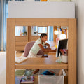 Young girl studying at a wooden loft-style desk with computer and lamp in a bright, organized home study space for remote learning