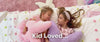 Various brightly decorated bedrooms with solid wood beds, bunk beds, and other bedroom furniture with families playing.
